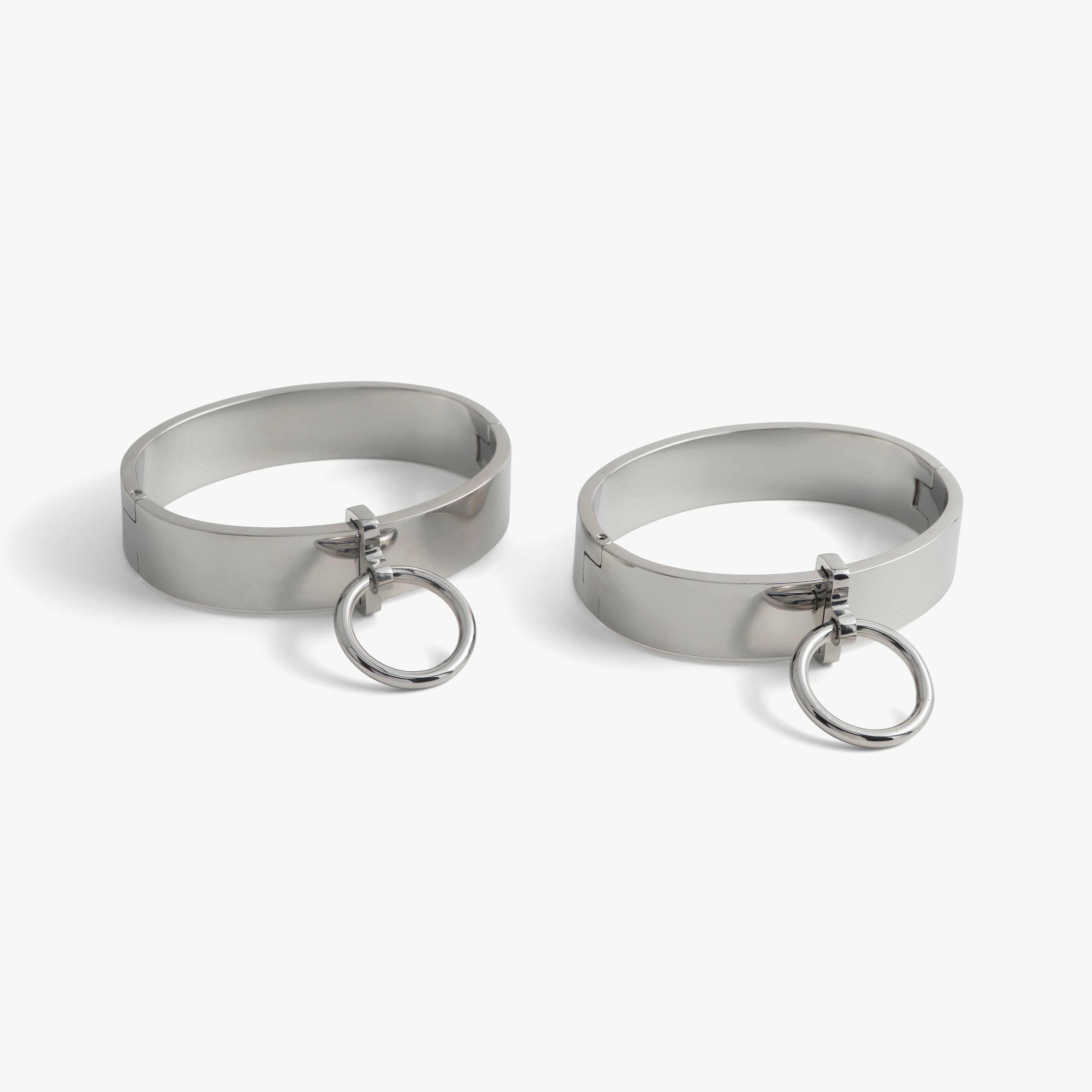 Pair of polished steel deSade ankle bands, each with a hanging O-ring