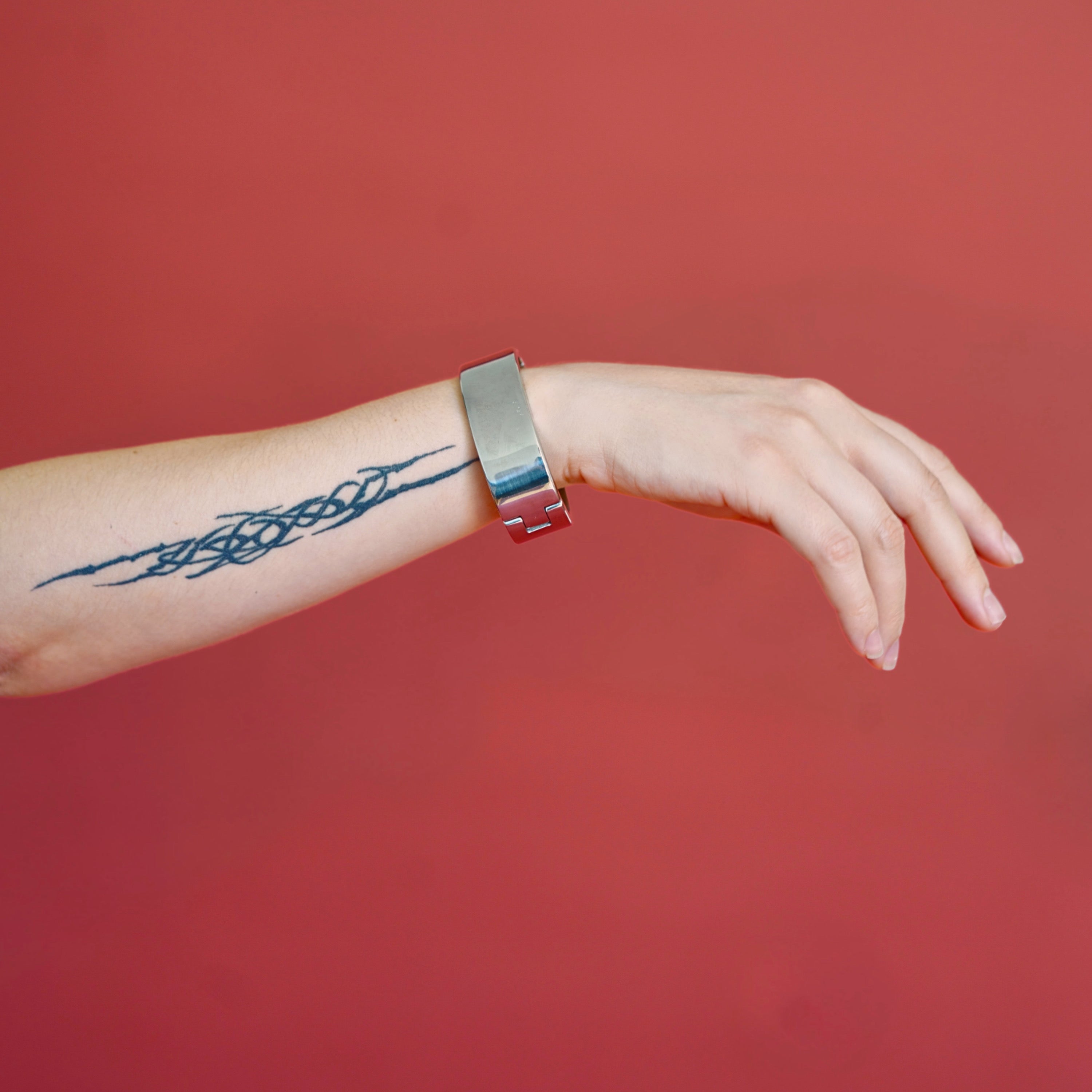 deSade silver wrist bracelet worn on a model's wrist against a red background