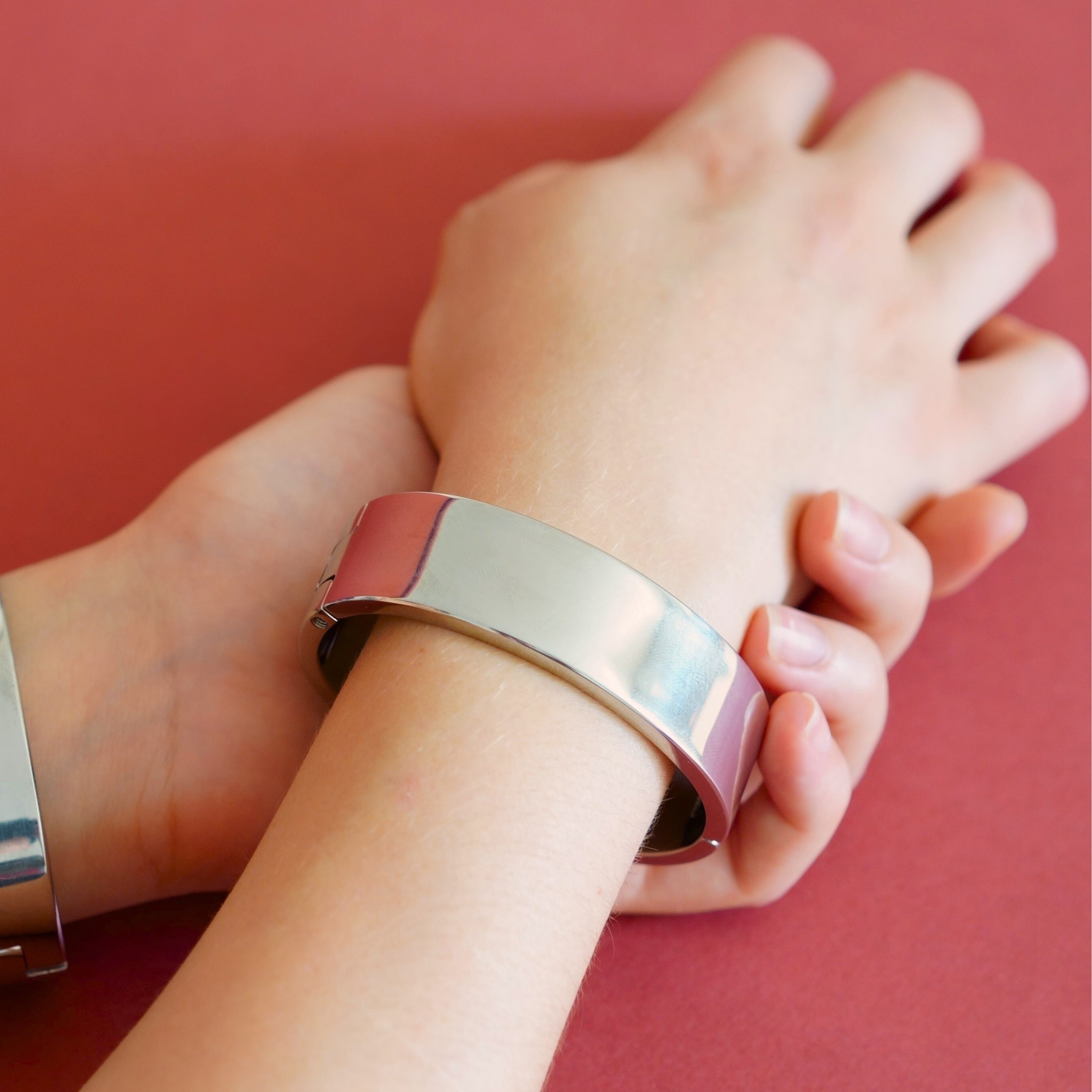deSade silver wrist bracelet worn on a model's wrist, alternate view on a red background