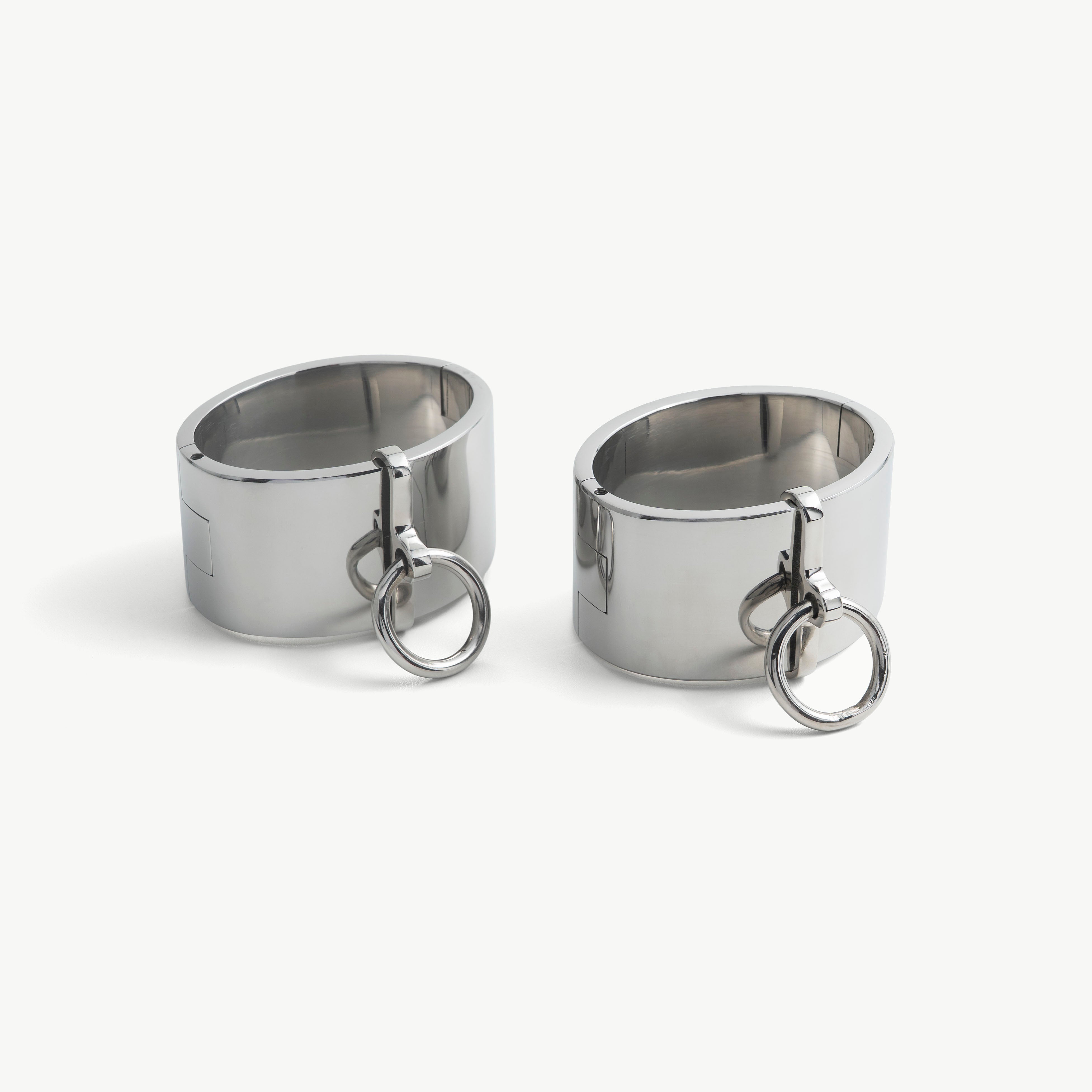 Pair of wide polished steel deSade wrist bands, each with a hanging O-ring