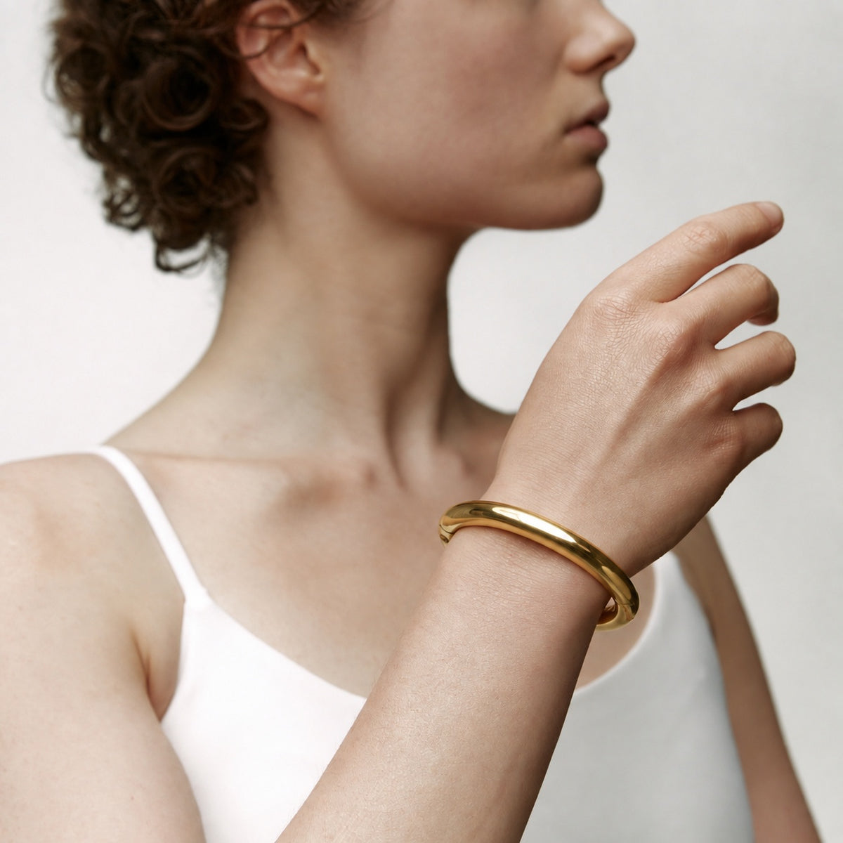 deSade gold wrist bracelet worn on the wrist, hand raised, side view